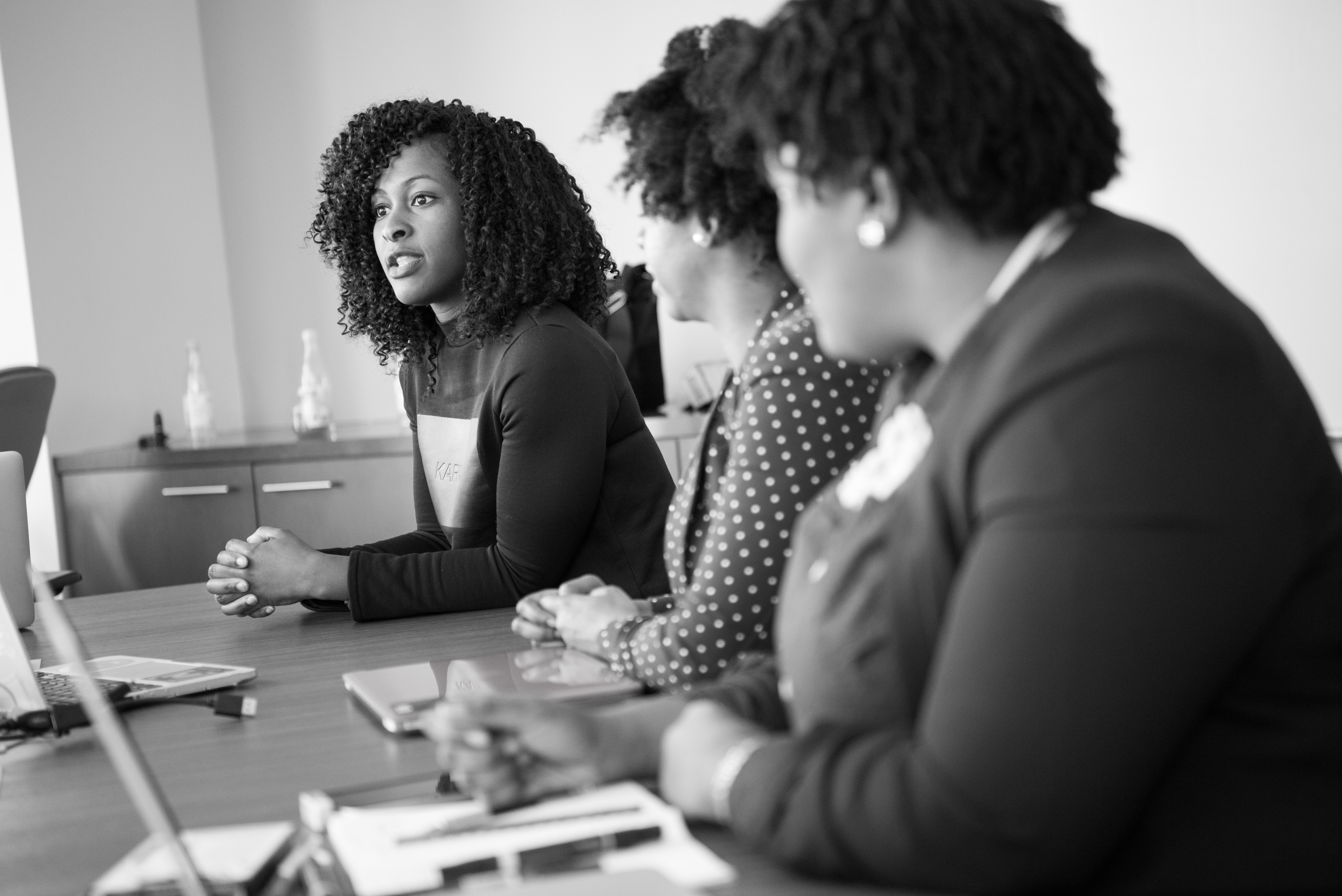 A and white photo of three black women sitting at a table talking.