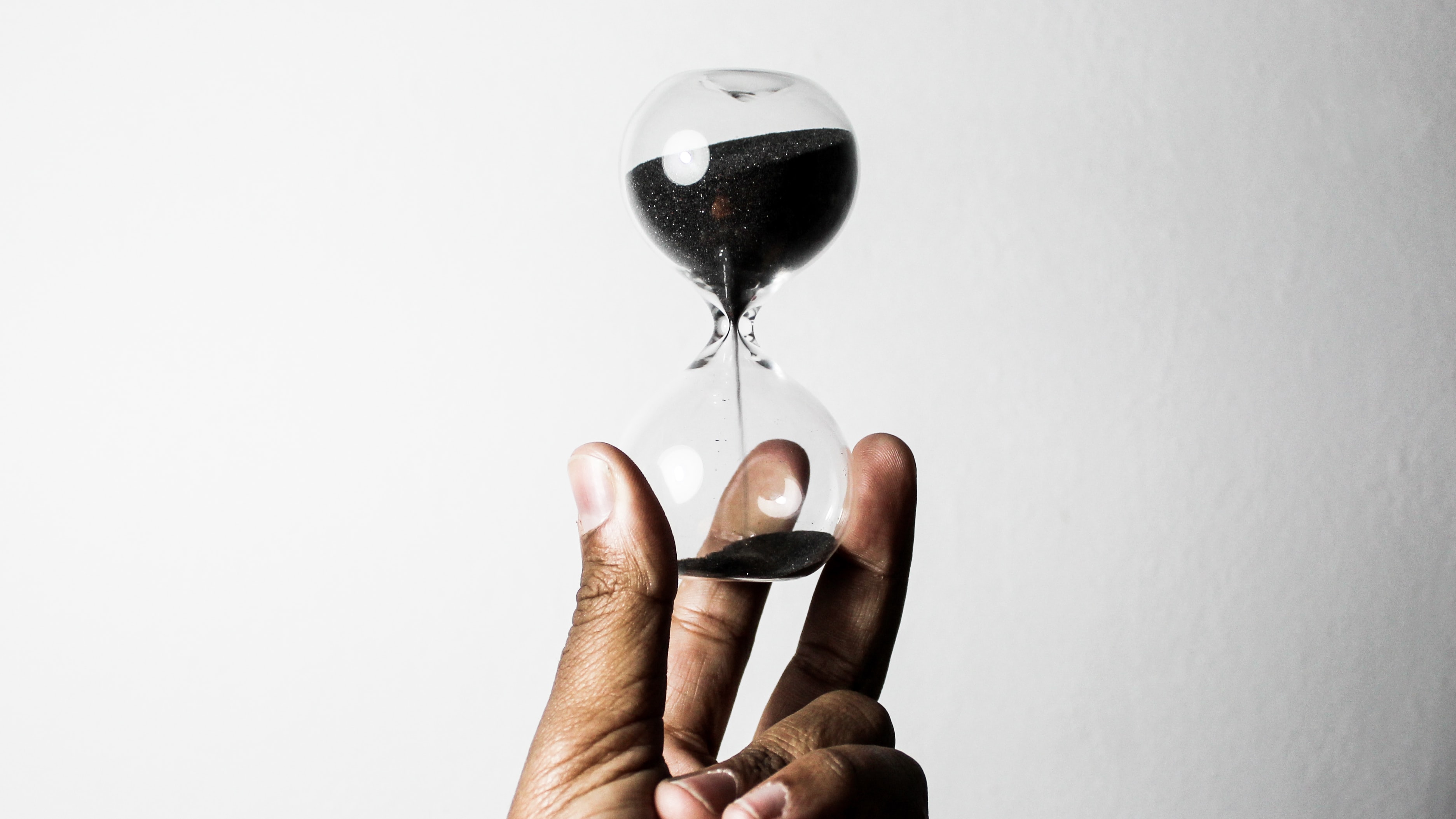 A black person's hand holding an hourglass.