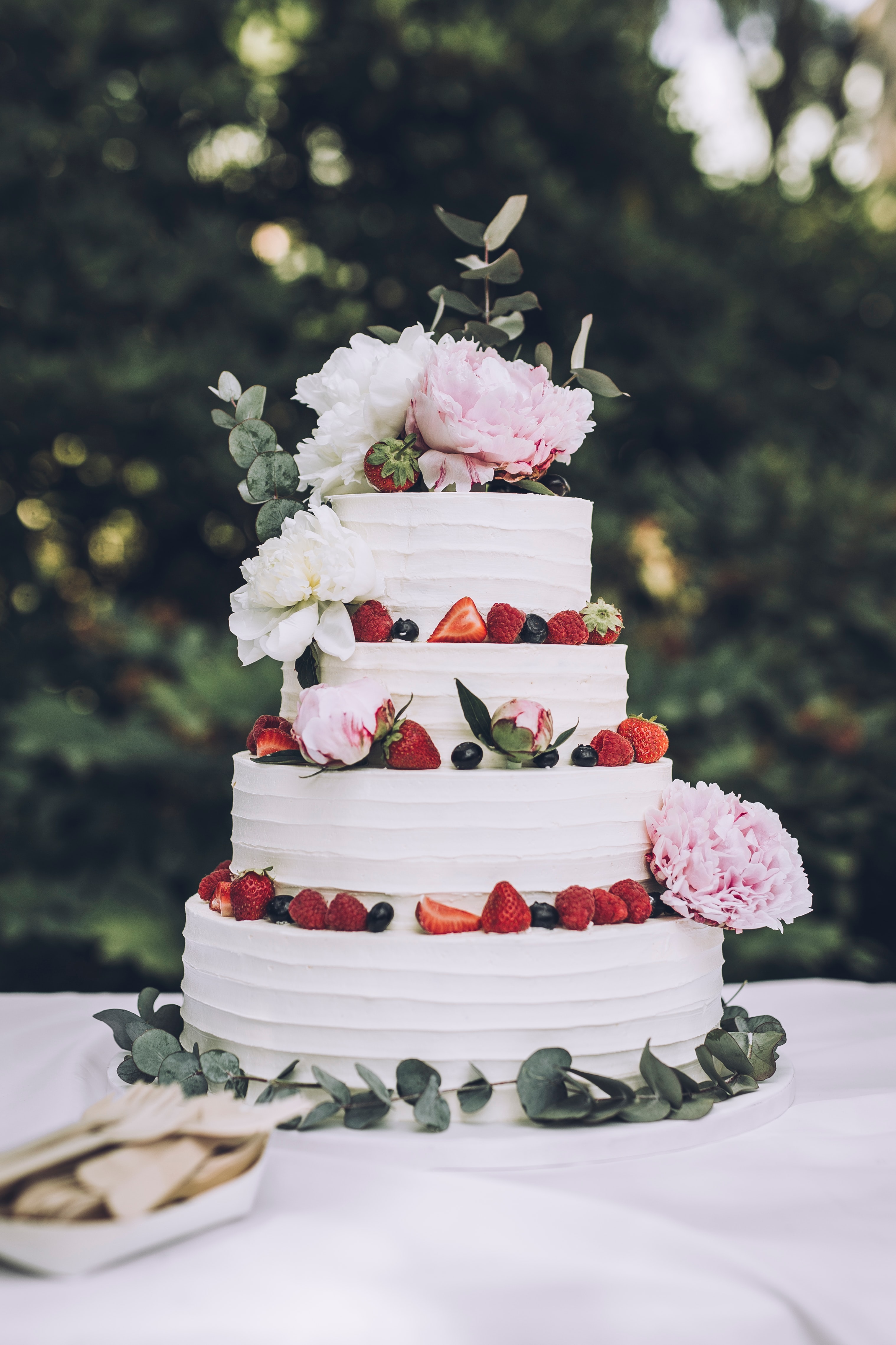 A white wedding cake decorated with strawberies, bluerries, eucalyptus leaves, and pink flowers